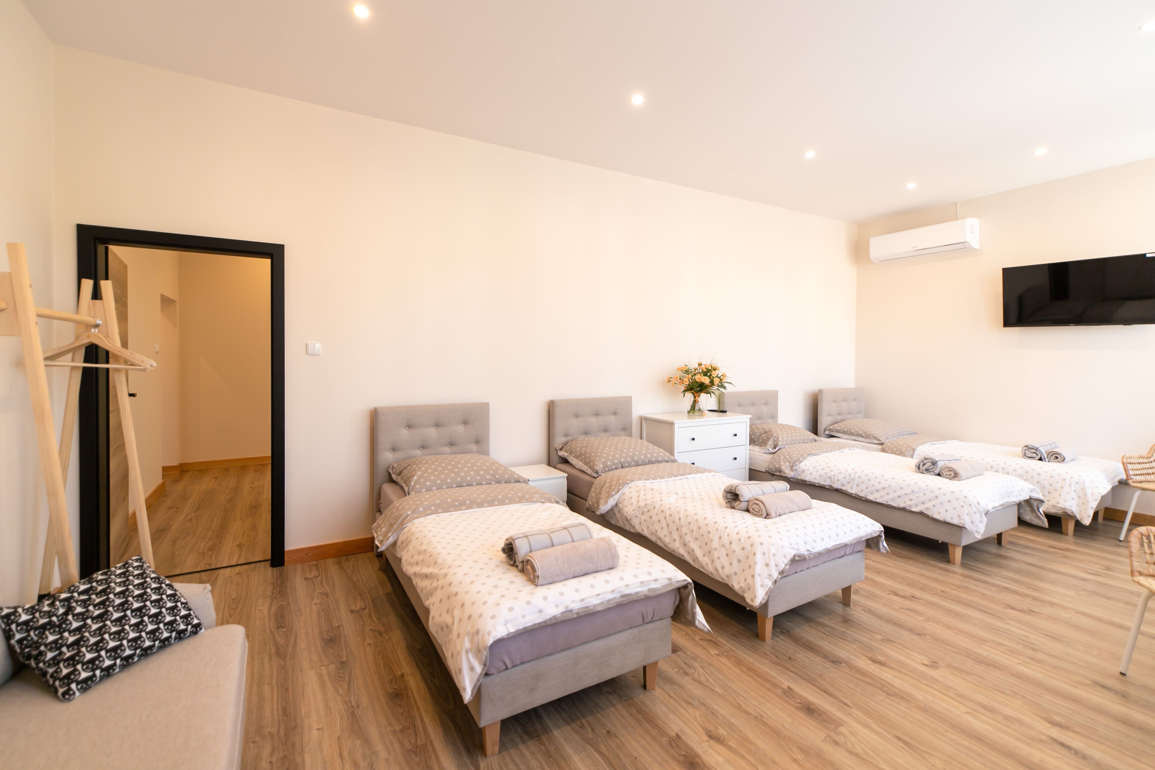 A hotel room with four single beds, a wooden floor, a flat-screen TV, and a wall-mounted air conditioner.