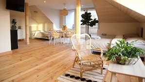 A spacious loft bedroom with a large bed, wooden flooring, a dining area with wicker chairs, and a TV mounted on the wall. - Dream Apart Apartamenty 51 (Ustron)