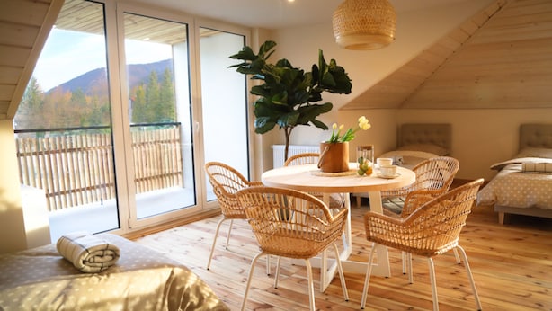 A cozy room with a wooden floor, a round table with chairs, a large potted plant, and a bed with a headboard. - Dream Apart Apartamenty 51 (Ustron)