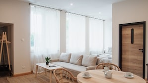 A modern living room with a sofa, a coffee table, wicker chairs, a round table with teapots, and a door. - Dream Apart Apartamenty 51 (Ustron)