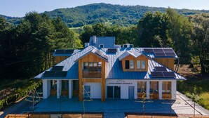 A modern building with solar panels, a wooden facade, and a view of a forested hill. - Dream Apart Apartamenty 51 (Ustron)