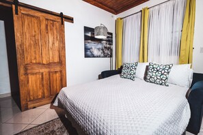 A bedroom with a bed, a wooden wardrobe, a painting, and curtains.