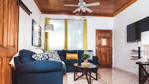 Sala de estar com sofá azul, mesa de centro, televisão e teto de madeira.