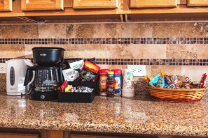 Una encimera de cocina con una cafetera, una cesta de aperitivos y diferentes productos de café.
