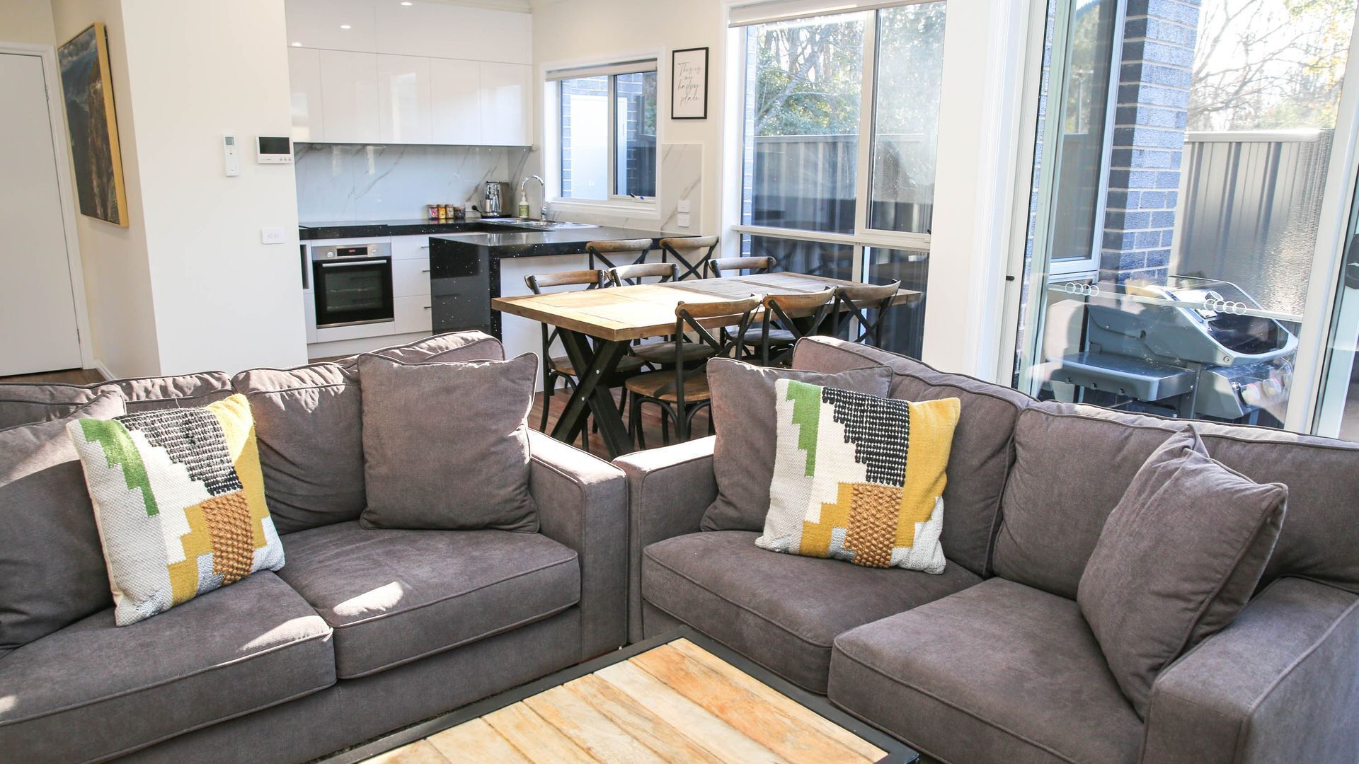 A modern living room with grey sofas, a wooden coffee table, and a dining area with a wooden table and chairs.