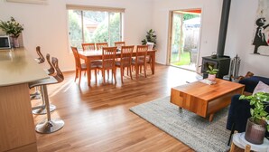Een moderne keuken met houten vloeren, een eethoek met een houten tafel en stoelen, een keukenbar met barkrukken, een groot raam en een open haard.