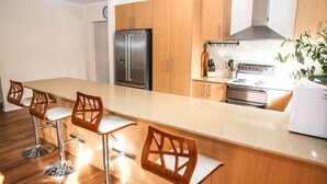 Een moderne keuken met houten kasten, een roestvrijstalen koelkast, een gasfornuis en barstoelen.