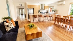 A modern living room with a sofa, coffee table, and a dining area with chairs and a table. - SHINE BRIGHT - Spacious family friendly group living in Bright (Bright)