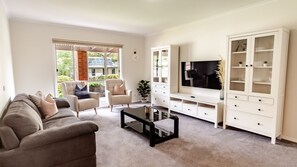 Ein Wohnzimmer mit einer Couch, Sesseln, einem Couchtisch, einem Fernseher und einem Schrank.