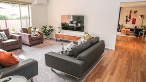 Een moderne woonkamer met een grijze bank, twee fauteuils, een salontafel en een televisie op een houten kast.