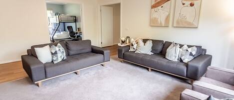 A living room with two grey sofas, a coffee table, and a rug. There are two doors leading to other rooms.