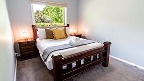 A neatly made bed with a wooden headboard, two bedside tables with lamps, and a window with a view of greenery. - SHINE BRIGHT - Spacious family friendly group living in Bright (Bright)