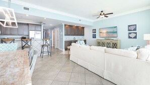 A spacious living area with a large beige sectional sofa, a kitchen with dark cabinets, and a dining area with bar stools. - Brand New Beach Front Condo with Lazy River! (Orange Beach)