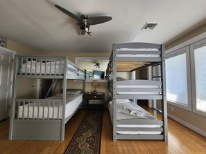 A bunk bed room with a ceiling fan, a desk with a lamp, and a window with blinds.