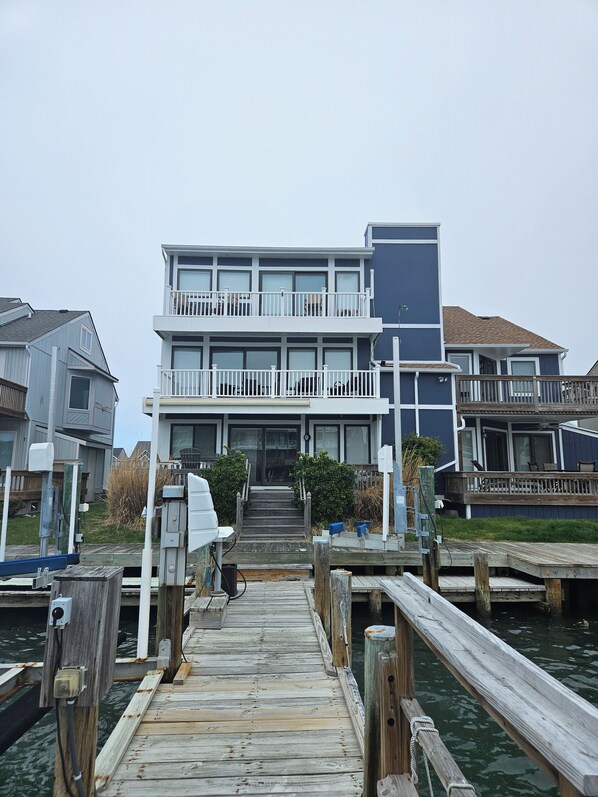 A waterfront property with a wooden dock leading to a two-story building with balconies.