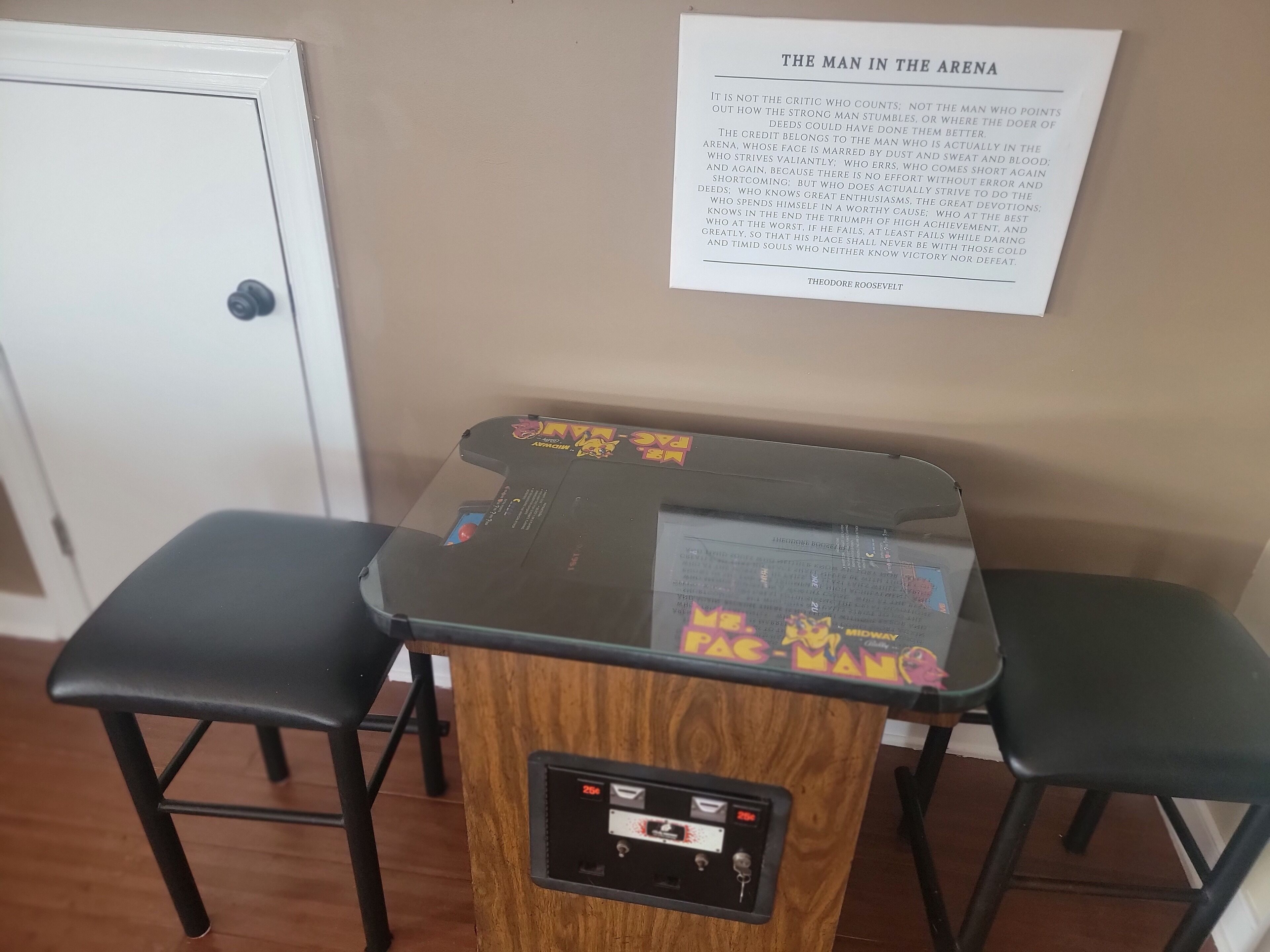 Une pièce avec une borne d’arcade Pac-Man, deux chaises noires et une porte.