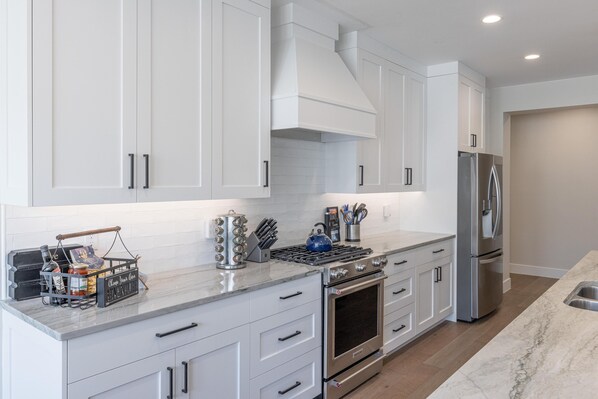 A modern kitchen with white cabinets, stainless steel appliances, and a marble countertop.