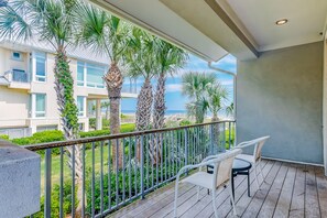 Enjoy the serene coastal view from this balcony with a view of palm trees and a distant building.