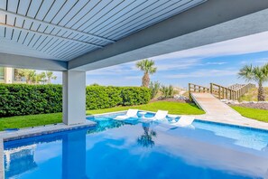 Relax by the clear pool surrounded by lush greenery and a wooden bridge.