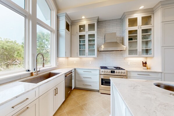 Enjoy cooking in this kitchen with a large window offering a view of the surrounding landscape, stainless steel stove, and ample counter space.