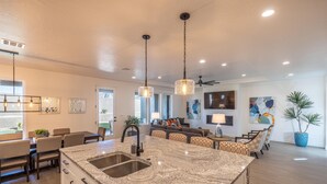Una cocina moderna con encimeras de granito, un lavamanos doble, iluminación colgante y una zona de comedor con sillas estampadas.