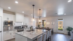 Una cocina moderna con armarios blancos, una isla central con taburetes de bar, electrodomésticos de acero inoxidable e iluminación colgante.