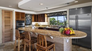 Cozinha moderna com uma ilha grande, forno embutido, frigorífico em aço inoxidável e banquetas de madeira.