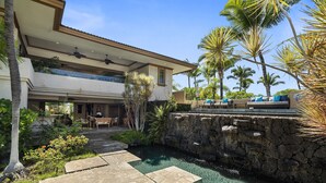 Uma casa moderna com um muro de pedra, piscina e palmeiras.