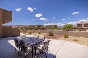A patio with a table and chairs, a clear sky, and distant buildings. - A Green Escape at The Ledges (St. George)