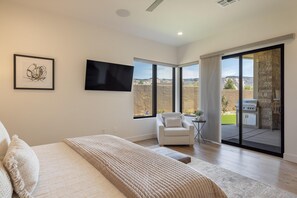 A bedroom with a bed, a chair, a TV, and a balcony with a grill. - The 19th Hole at The Ledges (St. George)