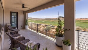 A covered outdoor area with wicker furniture, potted plants, and a view of a golf course. - Taking Flight (St. George)