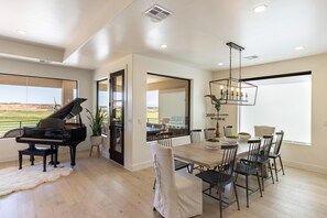 A spacious dining area with a piano, modern chandelier, and large windows offering a view. - Taking Flight (St. George)