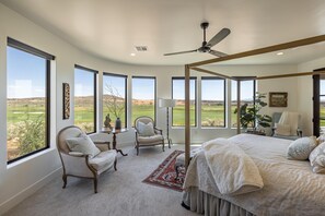 A bedroom with a large bed, a ceiling fan, and multiple windows offering a view of a golf course. - Taking Flight (St. George)