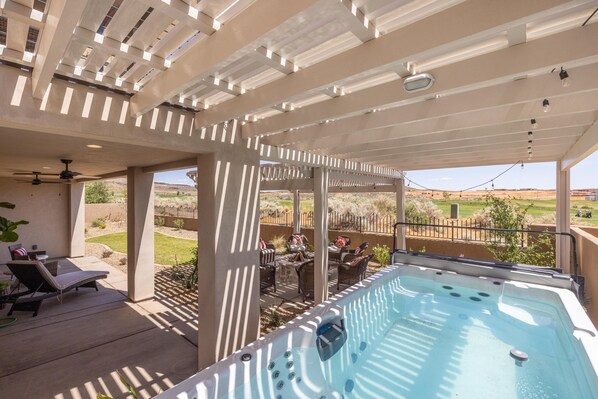 A covered outdoor area with a hot tub, lounge chairs, and a patio table. - Taking Flight (St. George)