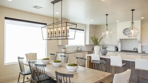 A modern kitchen with a dining area, featuring a wooden table, chairs, pendant lights, and built-in cabinets. - Taking Flight (St. George)