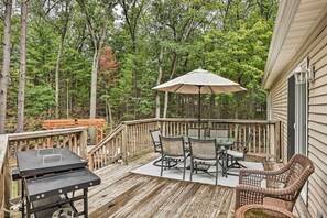 Enjoy al fresco dining on the deck, surrounded by a forested area, with a grill for outdoor cooking and a shaded dining table.