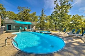 Relax by the oval-shaped pool surrounded by lounge chairs and a small building with a green awning.