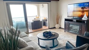 A living room with a sofa, armchairs, a coffee table, a TV, and a sliding glass door leading to an outdoor balcony. - Ocean View Oasis at Bajamar Resort (Ensenada)