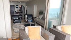A modern living room with wicker furniture, a sofa with a yellow cushion, and a dining area in the background. - Ocean View Oasis at Bajamar Resort (Ensenada)