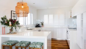 Una cocina moderna con armarios blancos, una isla central con taburetes, una lámpara colgante y vistas de la ciudad a través de amplios ventanales.