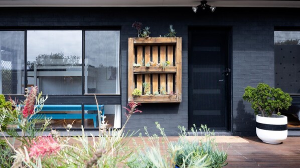 Una casa moderna con una jardinera de madera en la pared exterior, un banco y una planta en maceta.
