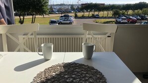 A balcony with a table, two chairs, and a view of a parking lot and trees.