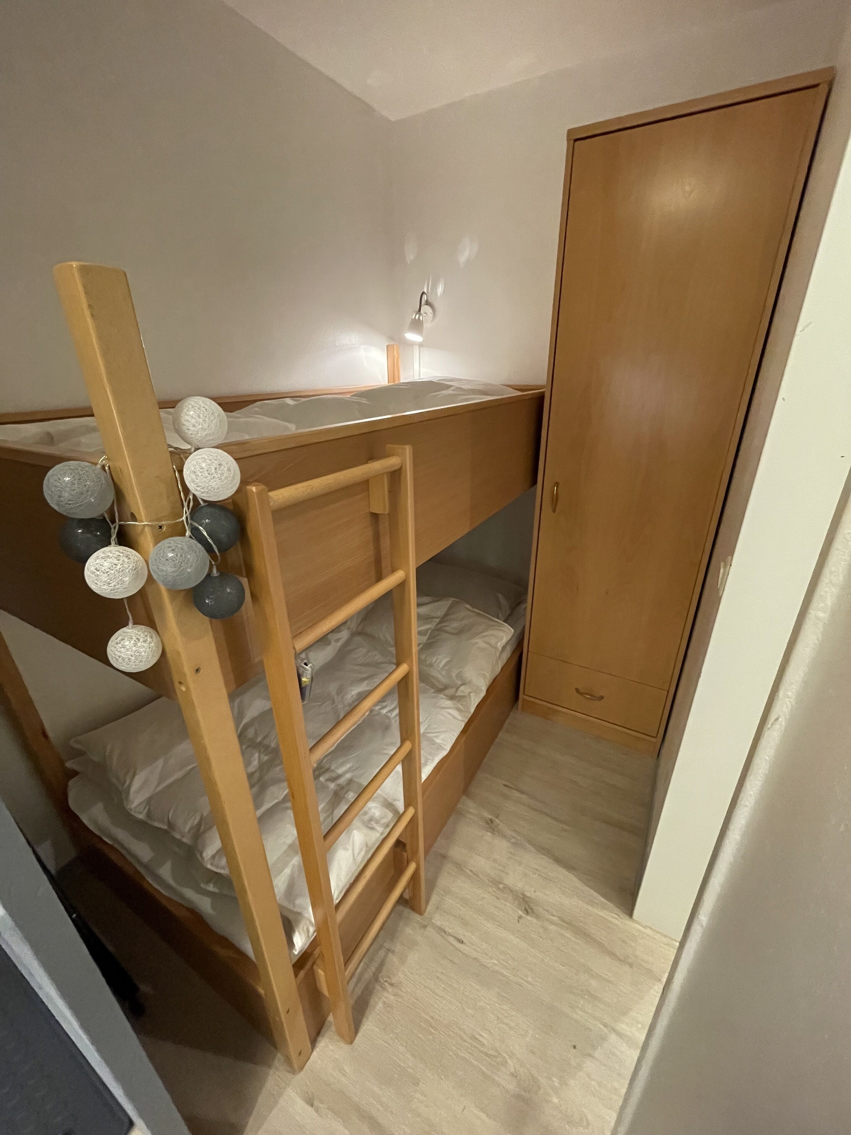 A bunk bed with a ladder, a bedside table, and a wardrobe in a room with wooden flooring.
