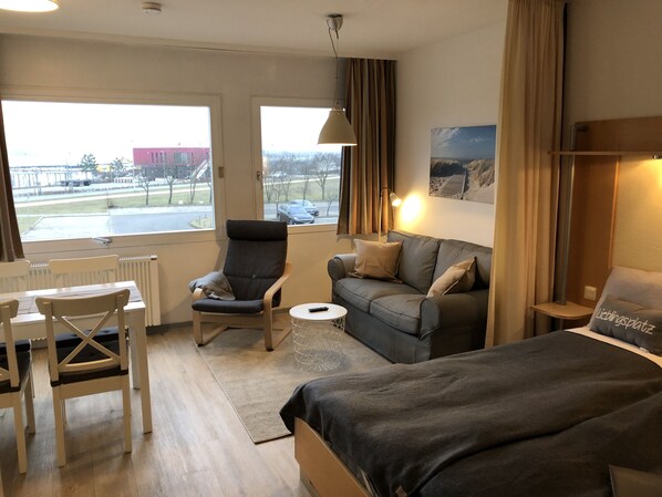 Une chambre d’hôtel avec un lit, un canapé, une chaise, une petite table et une vue sur l’extérieur.