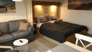 A modern hotel room with a sofa, two single beds, a small table, and a chair.