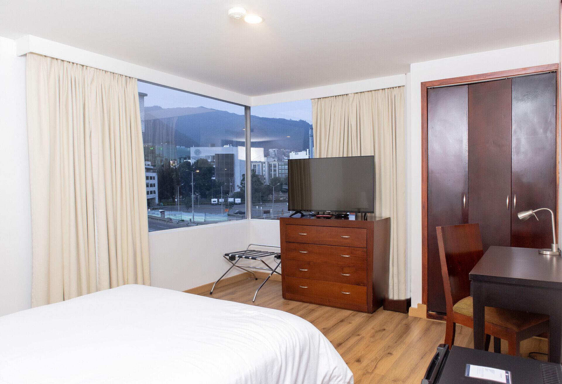 Una habitación de hotel con una cama, un televisor sobre un tocador de madera, un escritorio y una silla.