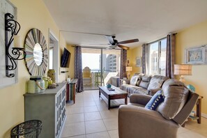 Ein Wohnzimmer mit einer Couch, einem Couchtisch und einem Deckenventilator. Blick auf einen Balkon mit Stuhl und Tisch.