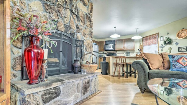 A living room with a stone fireplace, a red vase, a sofa, and a kitchen in the background.