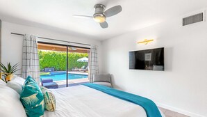 A bedroom with a bed, a ceiling fan, a TV mounted on the wall, and a view of an outdoor swimming pool. - Villa Del Sol – Modern Luxury on the Fairway (Palm Springs)