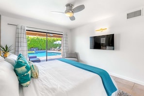 A bedroom with a bed, a ceiling fan, a TV mounted on the wall, and a view of an outdoor swimming pool.